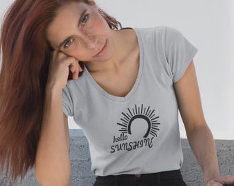May include: A light gray V-neck t-shirt with the text "hello sunshine" in a black, stylized font. The design includes a sunburst graphic. The shirt is made of a soft material.