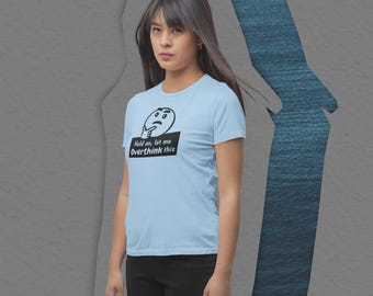 Op de afbeelding: Lichtblauw T-shirt met de zwarte tekst "Hold on, let me Overthink this". Het shirt heeft een afbeelding van een denkend gezicht. Het model draagt een zwarte broek.