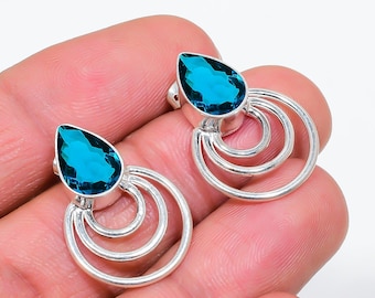 Puede incluir: Un par de pendientes de plata con gemas en forma de lágrima de color turquesa. Cada pendiente tiene un diseño circular de tres niveles. Los pendientes se muestran sobre un fondo neutro. Las gemas son de un vibrante color turquesa.