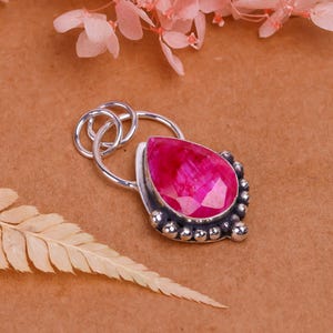 Puede incluir: Colgante de plata con una gran piedra preciosa rosa brillante en forma de lágrima facetada. La piedra está engastada en plata con pequeñas cuentas redondas de plata. El colgante tiene un lazo para una cadena.