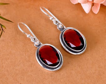 May include: A pair of silver drop earrings featuring oval, deep red gemstones. The earrings have a simple, elegant design with a polished finish. The gemstones are set in a silver bezel and are the focal point of the earrings.
