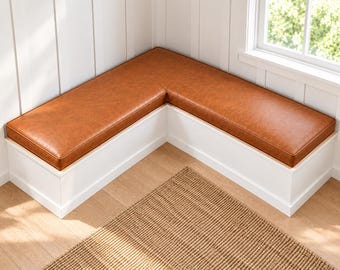 Pode incluir: Um banco de canto em forma de L com uma base de madeira branca sólida e uma almofada de assento lisa em pele sintética de cor castanha. O banco foi concebido para encaixar num canto, proporcionando uma superfície de assento contínua.