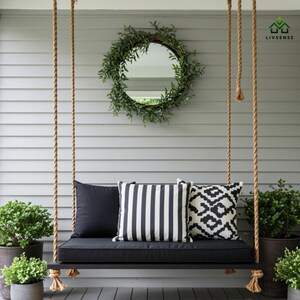 May include: A black wooden porch swing with a black cushion and three decorative pillows. The pillows have solid black, vertical stripes, and geometric patterns. The swing hangs from thick, natural-colored ropes. A round mirror with a green wreath hangs above the swing.