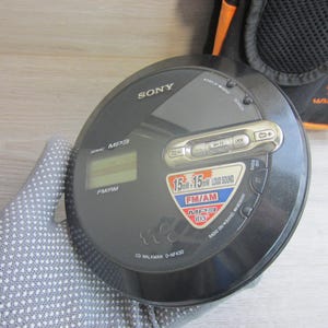 Może przedstawiać: Czarny odtwarzacz CD Walkman Sony D-NF430 z radiem FM/AM. Przenośny odtwarzacz CD ma cyfrowy wyświetlacz i przyciski sterowania. Urządzenie posiada funkcję głośnego dźwięku 15mW + 15mW, widoczne jest logo Walkman.