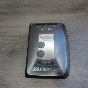May include: A silver and black Sony Walkman WM-FX173 portable cassette player. The device has a silver center panel with two gray buttons and the text "MEGA BASS". The Walkman has the text "WALKMAN FM/AM" and "ANTI-ROLLING".