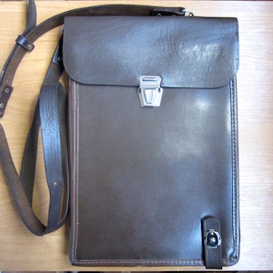 May include: A brown leather messenger bag with a flap closure and adjustable shoulder strap. The bag features a silver-colored clasp and buckle. The bag is approximately 12 inches tall and 10 inches wide.