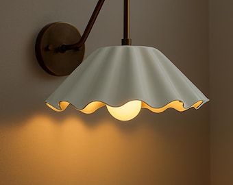 May include: A wall-mounted light fixture with a white, scalloped shade and a warm, glowing bulb. The fixture has a bronze-colored arm and a circular base, creating a vintage aesthetic. The light casts a soft, inviting glow on the wall.