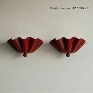 Könnte beinhalten: Zwei Wandleuchten in der Ausführung USC Cardinal. Jede Leuchte verfügt über einen breiten, gerüschten, fächerartigen Schirm mit glatter, matter Textur und einem kleinen, kugelförmigen Knopf an der Basis. Das Design ist symmetrisch und tiefrot.