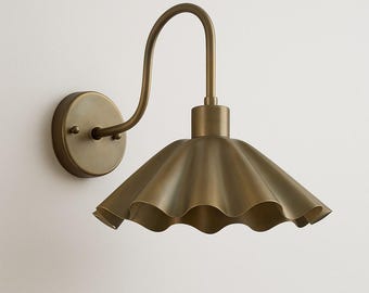 May include: A brass-toned wall sconce with a ruffled shade. The fixture has a curved arm and a circular base for mounting. The shade has a scalloped edge, adding a decorative touch to the lighting fixture.