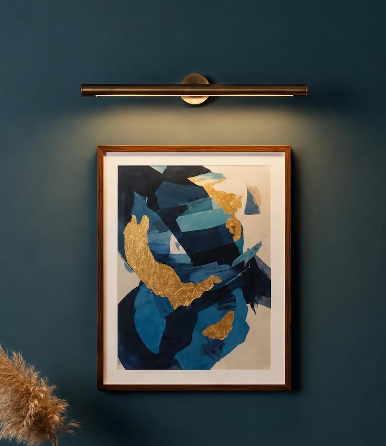May include: A rectangular framed wall art piece featuring abstract brushstrokes in shades of navy blue, light blue, and white, accented with gold leaf patches. Above the artwork is a horizontal, cylindrical metal wall light fixture.