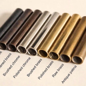 May include: A row of nine cylindrical metal tubes in various finishes, labeled as Matte black, Antique black, Blackened brass, Brushed chrome, Polished chrome, Brushed brass, Polished brass, Raw brass, and Antique patina, arranged side by side.