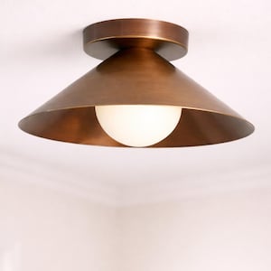 May include: A bronze ceiling light with a conical shade and a round base. The light fitting has a white, spherical bulb. The light is mounted on a white ceiling.