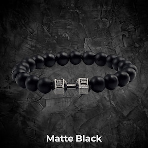 Op de afbeelding: Matzwarte kralenarmband met een zilveren halterbedel. De armband is gemaakt van ronde, matzwarte kralen en heeft een haltervormige bedel in het midden. De tekst "Matte Black" staat onderaan de afbeelding.