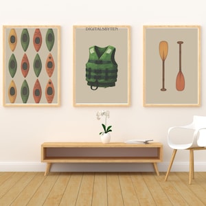 May include: Three framed art prints featuring kayaking and boating themes. One print displays a pattern of kayaks in yellow, green, and orange. Another shows a green life vest. The third print depicts two paddles. The text "DIGITALSBYTEN" is visible.