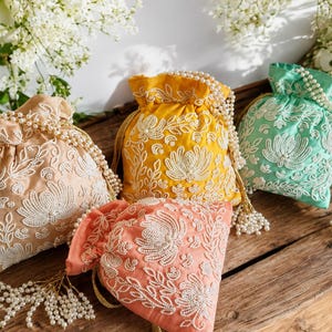 Könnte beinhalten: Vier Beutel mit Kordelzug in Pfirsich, Gelb, Minzgrün und Koralle, jeweils mit aufwendigen weißen Perlenstickereien in Blumenmustern. Die Taschen haben perlenartige Kordelzüge mit hängenden Quasten und bestehen aus einem glatten Stoff.