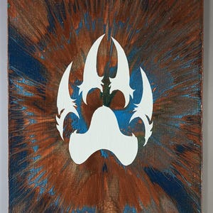 Puede incluir: Una pintura sobre lienzo con un diseño de huella de pata blanca sobre un fondo de colores marrones, azules y cobrizos arremolinados. La obra de arte tiene una apariencia texturizada, con los colores irradiando hacia afuera desde el centro.