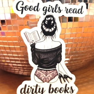 May include: A sticker with the text "Good girls read dirty books." The sticker features an illustration of a person with their back to the viewer, reading a book, wearing a black sweater and pink lace underwear.