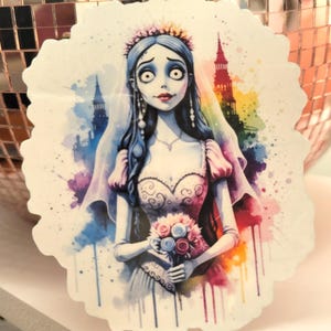 Puede incluir: Una pegatina con una ilustración en acuarela de una novia con piel pálida, cabello azul y una corona floral. Lleva un vestido blanco y sostiene un ramo de rosas. El fondo tiene salpicaduras coloridas y un edificio arcoíris.