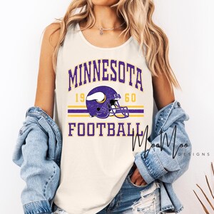 May include: Cream-colored tank top featuring the words "MINNESOTA FOOTBALL 1960" in purple and gold. A purple football helmet graphic is centered on the shirt. The tank top is sleeveless.