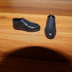 K&ouml;nnte beinhalten: Ein Paar schwarze Lederschuhe mit Schnallen. Die Schuhe befinden sich auf einer Holzoberfl&auml;che.