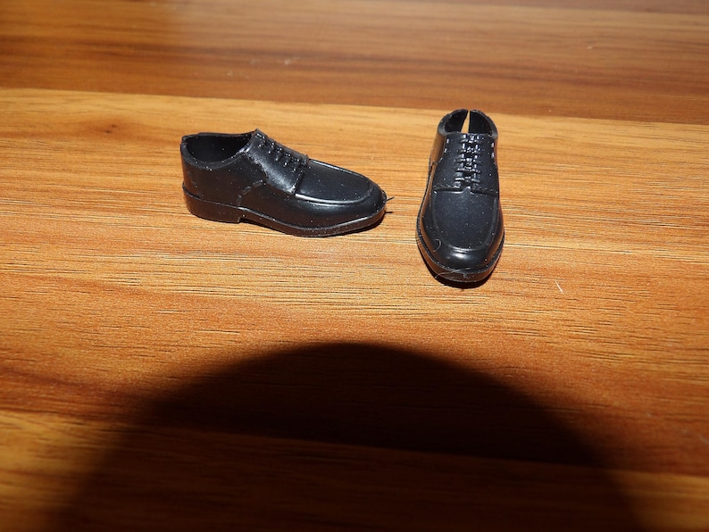 K&ouml;nnte beinhalten: Ein Paar schwarze Lederschuhe mit Schnallen. Die Schuhe befinden sich auf einer Holzoberfl&auml;che.
