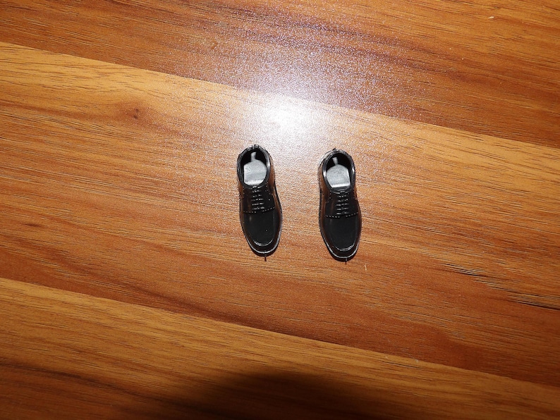 K&ouml;nnte beinhalten: Zwei schwarze Lederschuhe mit Schn&uuml;rsenkeln. Die Schuhe befinden sich auf einer Holzoberfl&auml;che.