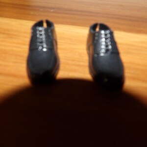 K&ouml;nnte beinhalten: Ein Paar schwarze Lederschuhe mit Schn&uuml;rsenkeln. Die Schuhe sind abgenutzt und haben eine abgewetzte Optik.