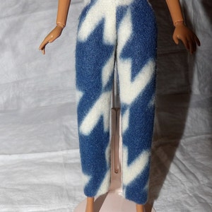 May include: Blue and white patterned pants. The pants have a high waist and a straight leg. The pattern is a repeating design of white shapes against a blue background. The pants are made of a soft, fuzzy material.