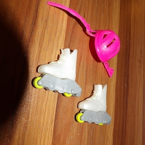 May include: A pair of white toy roller skates with gray bases and yellow wheels. A pink helmet with a strap is also present. The items are arranged on a wooden surface.