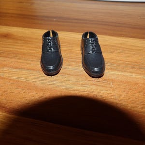 K&ouml;nnte beinhalten: Ein Paar schwarze Lederschuhe mit Schn&uuml;rsenkeln. Die Schuhe haben eine abgerundete Spitze und einen niedrigen Absatz.
