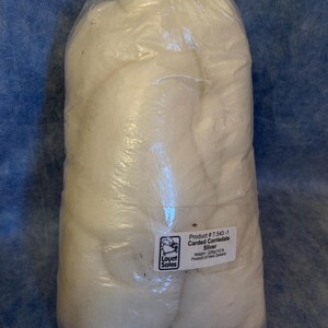 May include: A clear plastic bag containing white carded Corriedale sliver wool. A white label on the front reads: Product # 7.543-1, Carded Corriedale Sliver, Weight - 225gr/1/2 lb, Product of New Zealand, with a Louet Sales logo.