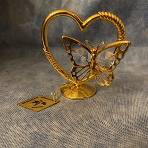 May include: A gold-plated butterfly figurine with a crystal body, set within a heart-shaped frame. The frame has a twisted rope design. A tag reads "24K Gold Plated" and "KD & CLINC."