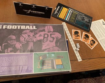 May include: A vintage Thinking Man's Football board game with a colorful game board, dice, and player pieces. The game board features a photo of football players in action. The game includes a rule book and a play selection card.