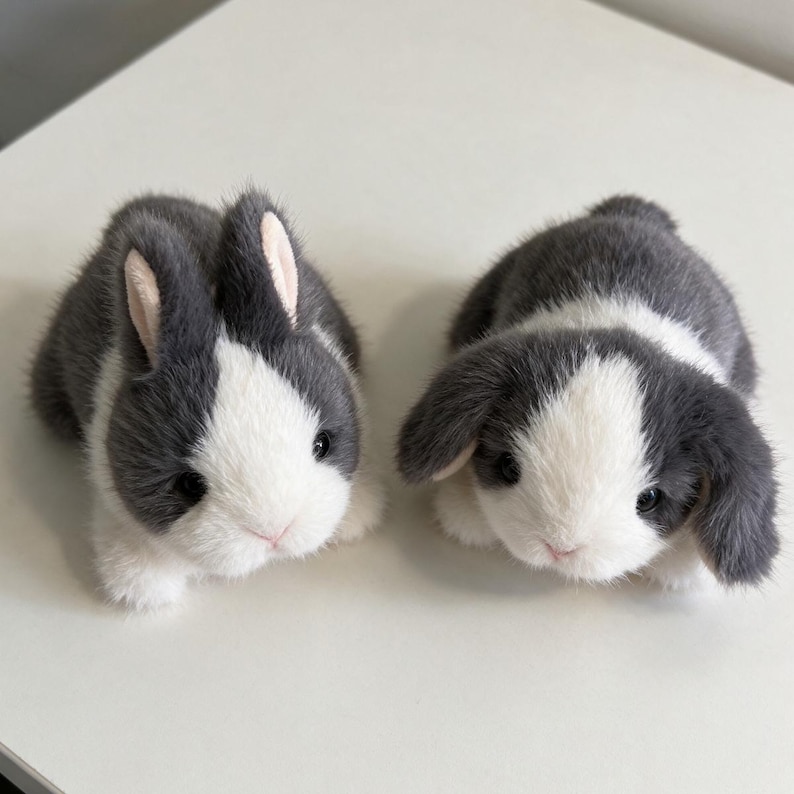 May include: Two plush rabbit figurines with soft, faux fur in shades of dark gray and white. One rabbit features upright ears with pink inner linings, while the other is a lop-eared rabbit with long, drooping ears. Both have dark eyes.
