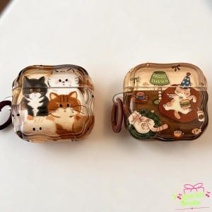May include: Two square, wavy-edged protective cases for wireless earbuds. The left case features a group of illustrated cats in black, white, and brown. The right case displays a brown scene with a cat wearing a party hat, eating a burger.