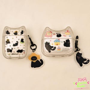 May include: Two clear, cat-shaped protective cases for wireless earbuds. The left case features small black cat illustrations and the text "Black cat". The right case displays larger black cat graphics, a house, and a cake. Both include black clips.