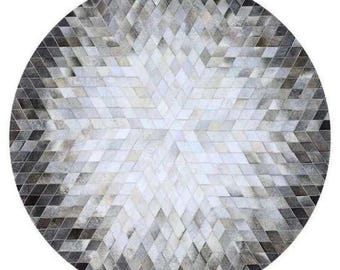 May include: A round rug with a geometric pattern. The rug features a diamond pattern in shades of white, gray, and black. The design radiates from the center, creating a starburst effect. The rug is likely made of a soft material, suitable for a living room or bedroom.