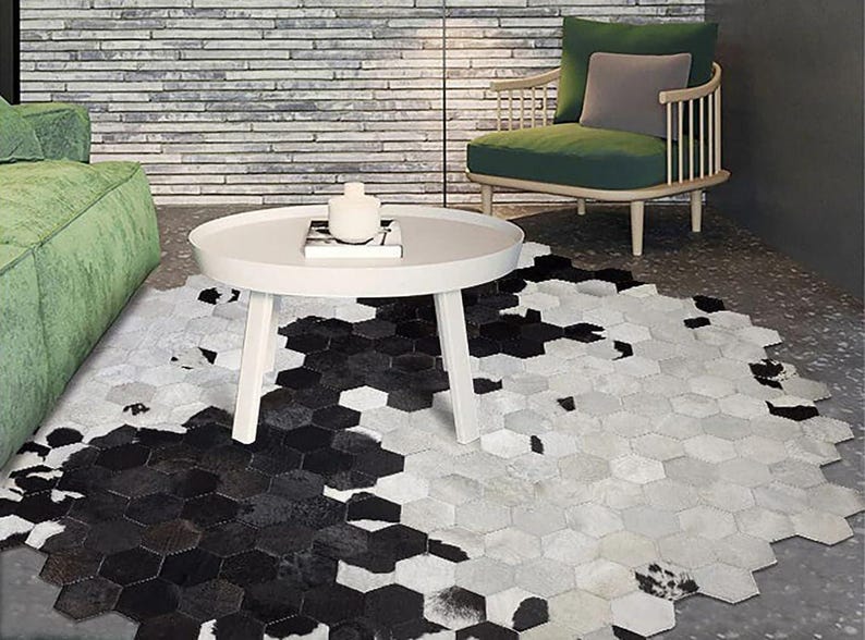 May include: A modern living room scene featuring a white round coffee table and a unique hexagonal rug. The rug has a striking black and white cowhide pattern. A green sofa and chair add color to the room.