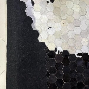 May include: A cowhide rug with a geometric pattern. The rug features a patchwork design of hexagonal shapes in black, white, and shades of gray. The rug has a black backing.