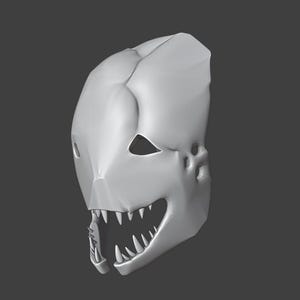 May include: A gray, stylized mask with sharp teeth and pointed ears. The mask has a smooth, matte finish and a menacing appearance, with triangular eye holes and a prominent jawline. The overall design suggests a creature or monster theme.