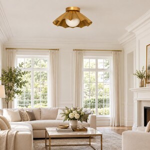 May include: A flush mount ceiling light fixture featuring a wide, scalloped, metallic gold shade with a central, spherical, frosted white glass globe bulb, providing a downward-facing light source in a room with high ceilings and neutral decor.