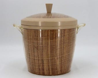 May include: A vintage ice bucket with a woven brown pattern. The bucket has a matching lid and a small handle on top. Clear plastic handles are on either side of the bucket.