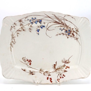 May include: A rectangular white ceramic serving platter with scalloped edges, featuring a delicate botanical illustration of brown stems, blue bell-shaped flowers, and small red berries arranged in a curved pattern across the surface.