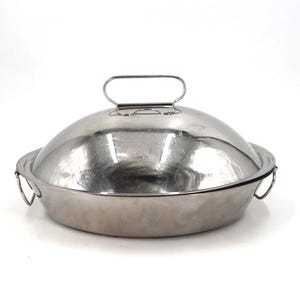 May include: A stainless steel cloche with a domed lid and a handle. The round base has two side handles. The lid has a handle for easy lifting. The cloche is designed to cover food.