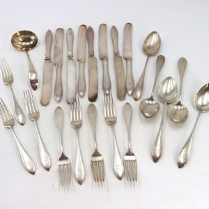May include: A collection of silver-toned metal flatware including various forks, knives, and spoons. The set features multiple dinner forks, salad forks, table knives, soup spoons, and a single round ladle, all arranged in a loose group on a surface.