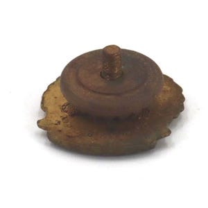 May include: A vintage-style, bronze-colored pin with a threaded post and a circular base. The pin has a detailed, possibly floral, design around the edge. The pin is set against a white background.