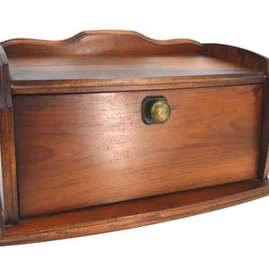 May include: A wooden bread box with a curved top and a brass knob. The box is made of dark brown wood and has a rectangular shape. The bread box has a small shelf at the bottom and a decorative edge.