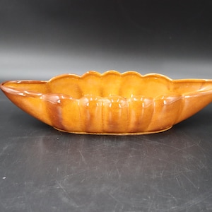 May include: A vintage, oblong-shaped ceramic dish with a scalloped rim. The dish is a warm, earthy brown color with darker brown accents. The interior has a glossy finish. This decorative piece could be used for serving or display.