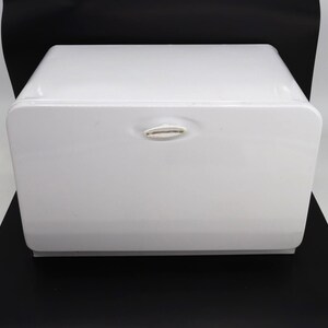 May include: A rectangular white bread box with a smooth, glossy finish and rounded corners. The front panel features a centered, oval-shaped handle with a slightly recessed design, providing a clean and simple aesthetic for kitchen storage.