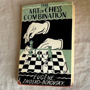 May include: Vintage book titled "The Art of Chess Combination" by Eugene Znosko-Borovsky. The cover features a black and white illustration of chess pieces on a checkered board, with hands reaching down. The book has a light blue and black color scheme.